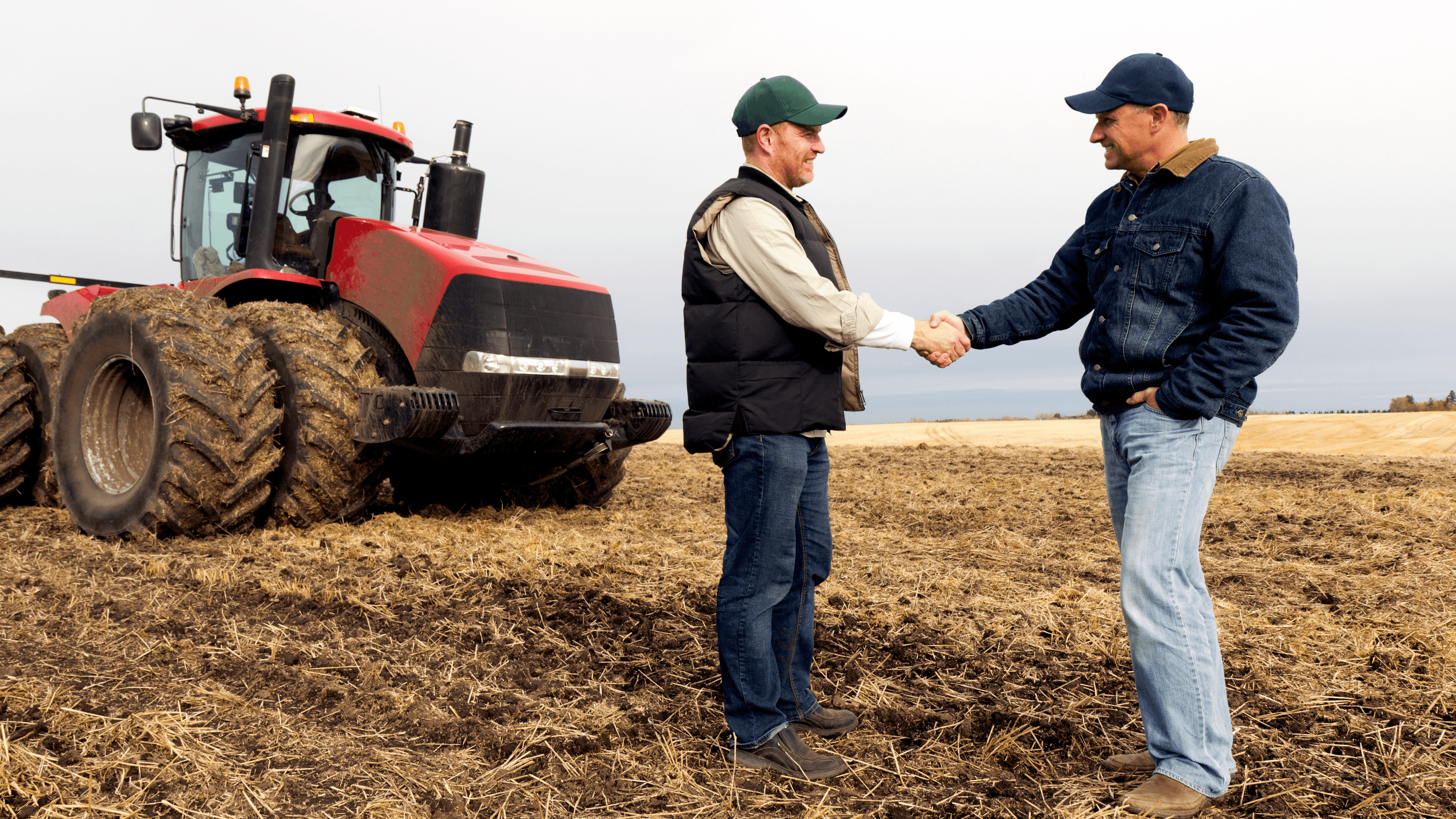 Farmers shaking hands near a tractor in a field.